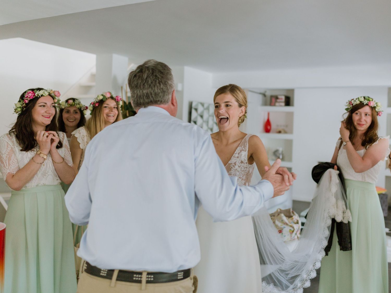 La mariée, vêtue d'une robe en dentelle blanche, rit avec ses demoiselles d'honneur en robes menthe et couronnes de fleurs