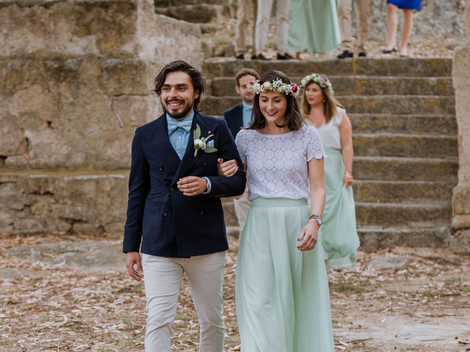 La mariée, vêtue d'une jupe vert menthe et d'une couronne de fleurs, accompagne le marié en costume bleu marine lors d'une cérémonie