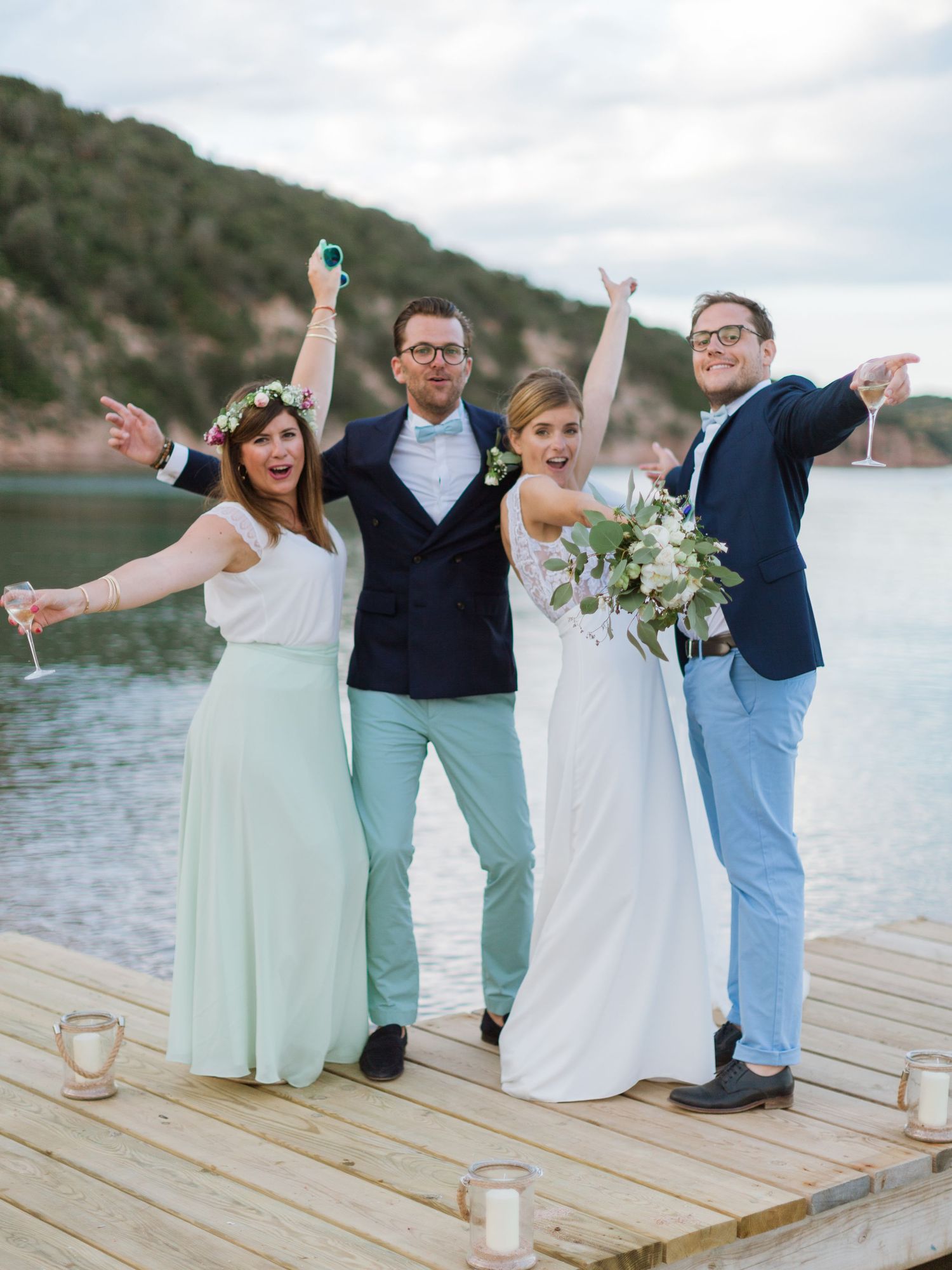 Un cortège de mariage célèbre sur un quai, levant ses verres avec un lac et des collines pittoresques en arrière-plan.