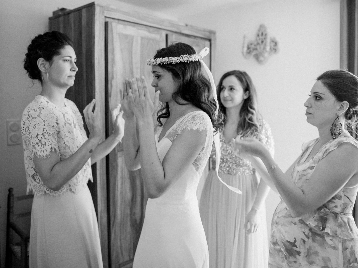 Black and white photo of a bride and three bridesmaids preparing for the wedding ceremony indoors.