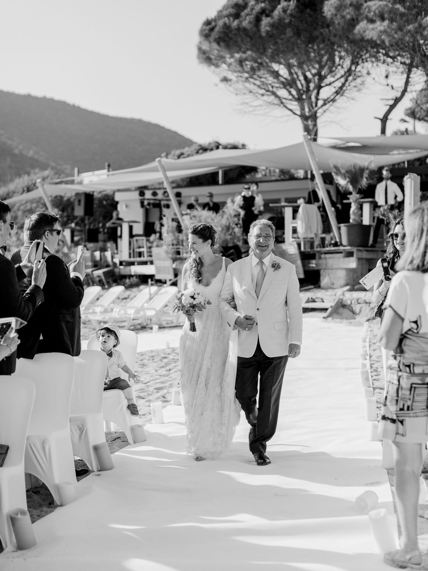 Photo en noir et blanc d'une mariée descendant l'allée au bras de son père lors d'une cérémonie de mariage en plein air à Ajaccio au weekend