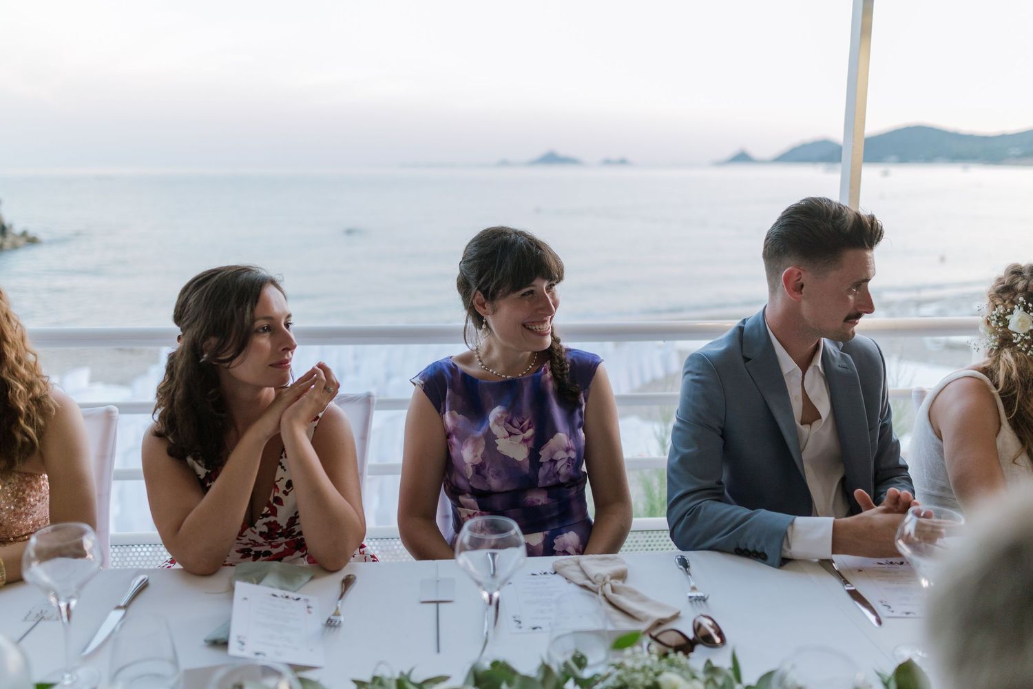 Des invités de mariage riant et célébrant autour d'une table de réception en plein air, au bord de la mer et avec vue sur l'océan, au crépus