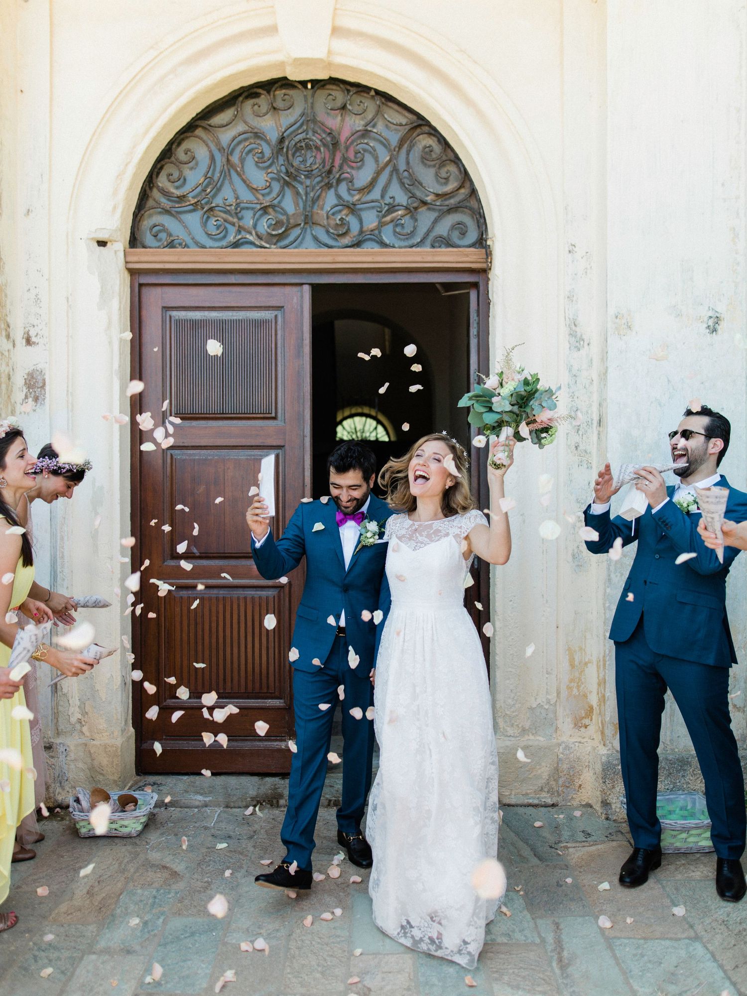 Bride and groom exit church doors as guests toss flower petals in joyful wedding celebration.