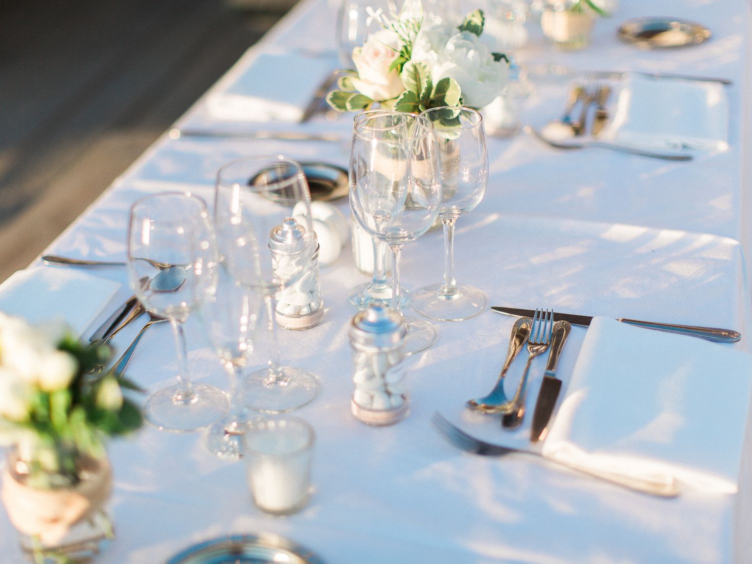 Élégante décoration de table pour un mariage, avec nappes blanches, verres à vin en cristal, couverts en argent et centres de table floraux