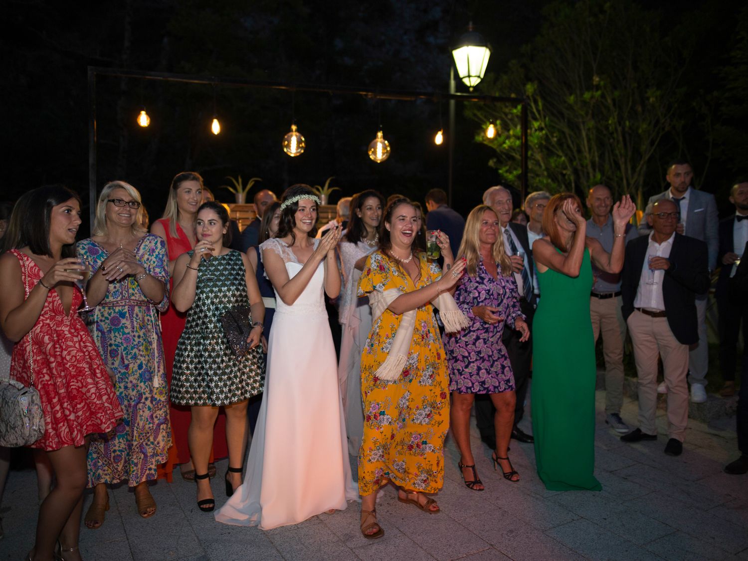 La mariée en robe blanche célèbre son mariage avec ses invités lors d'une réception en plein air sous des guirlandes lumineuses.