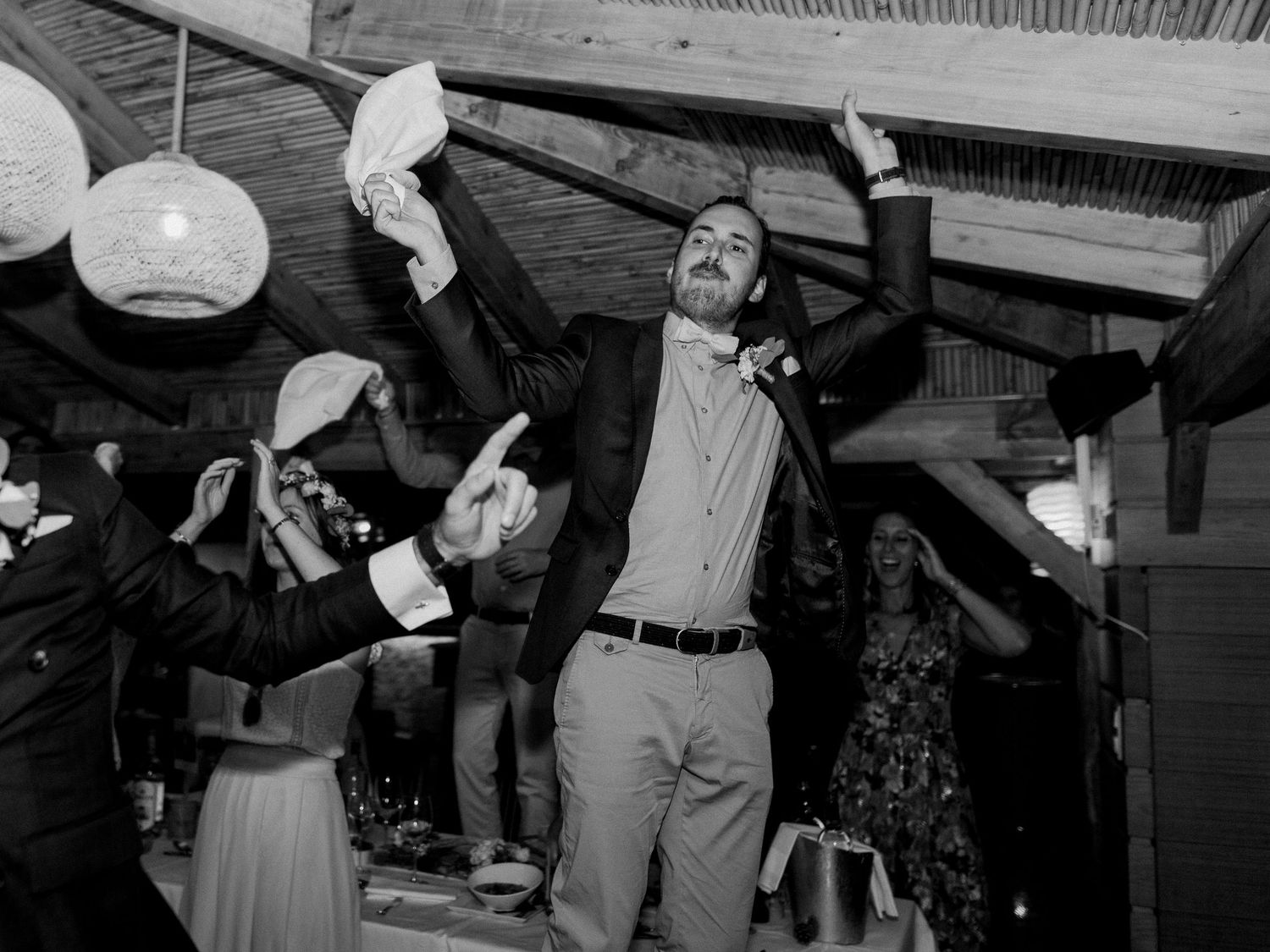 Photo en noir et blanc d'un marié dansant joyeusement avec ses invités lors d'une réception de mariage animée.