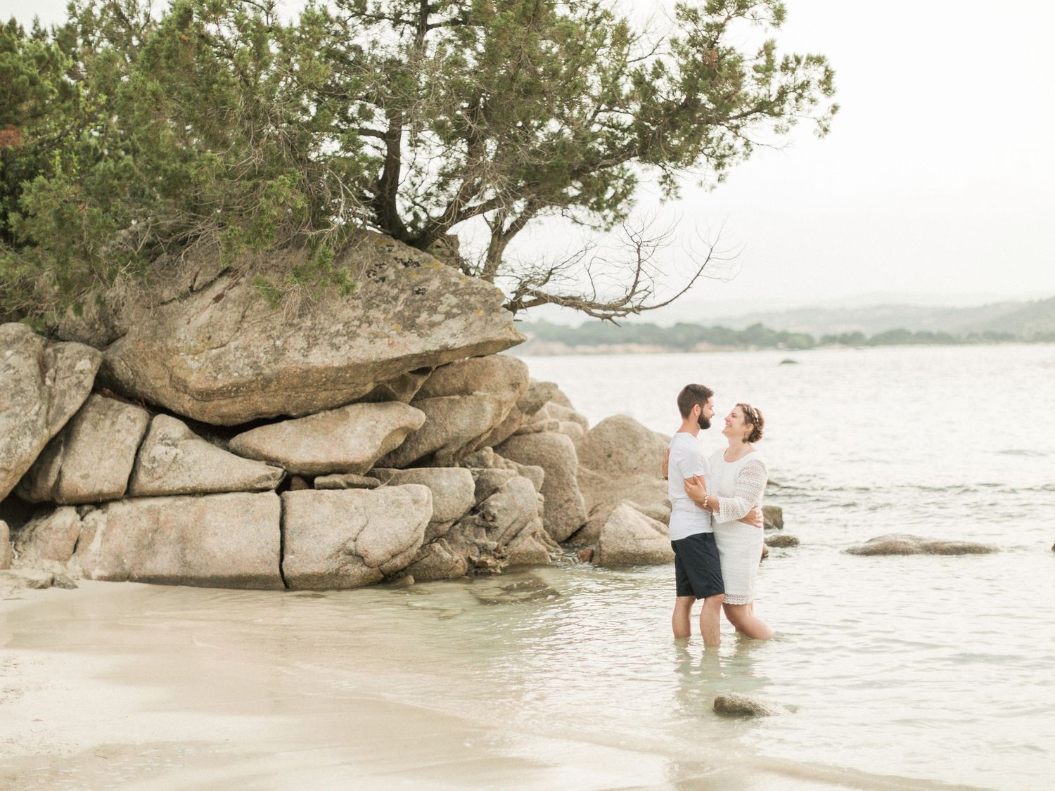 Un couple romantique se tient côte à côte dans l'eau peu profonde, près de gros rochers côtiers sur une plage à Palombaggia  porto-vecchio