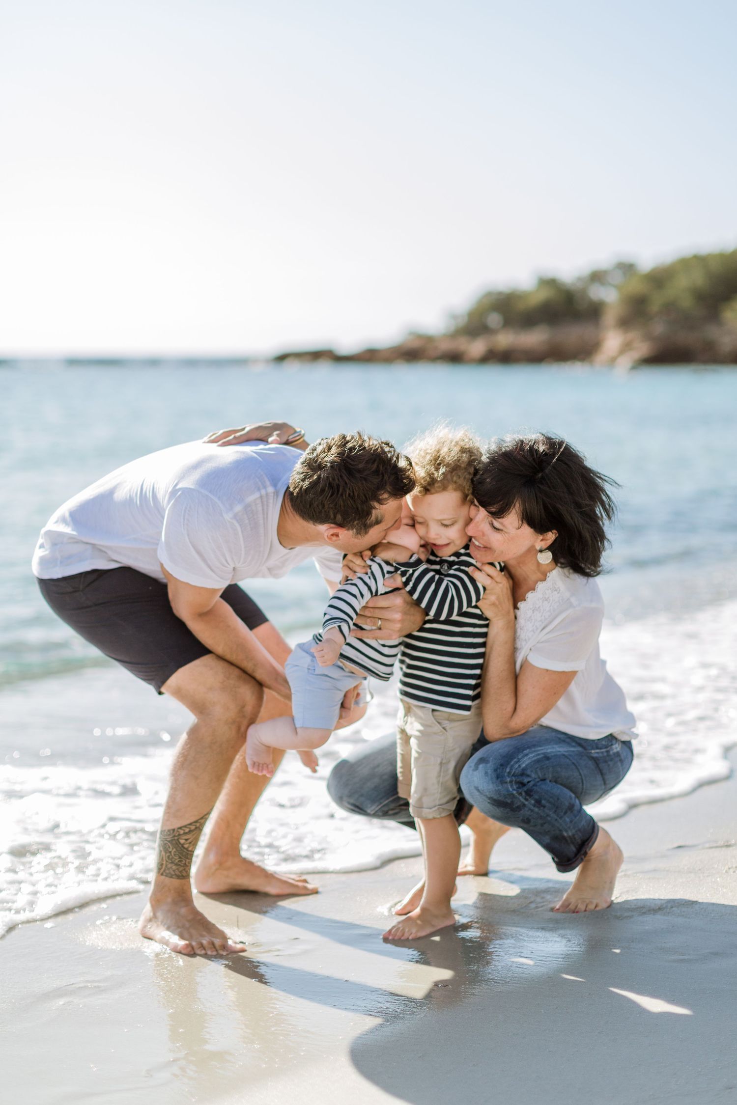 Une famille heureuse de quatre personnes, les parents embrassant leur jeune enfant sur le rivage ensoleillé de la plage de Palombaggia Corse