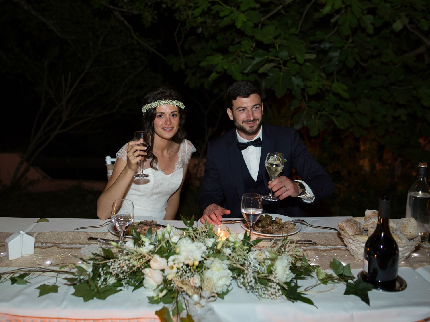 Les mariés trinquent au champagne à la table de réception de mariage en plein air, ornée d'un centre de table floral blanc, en soirée.