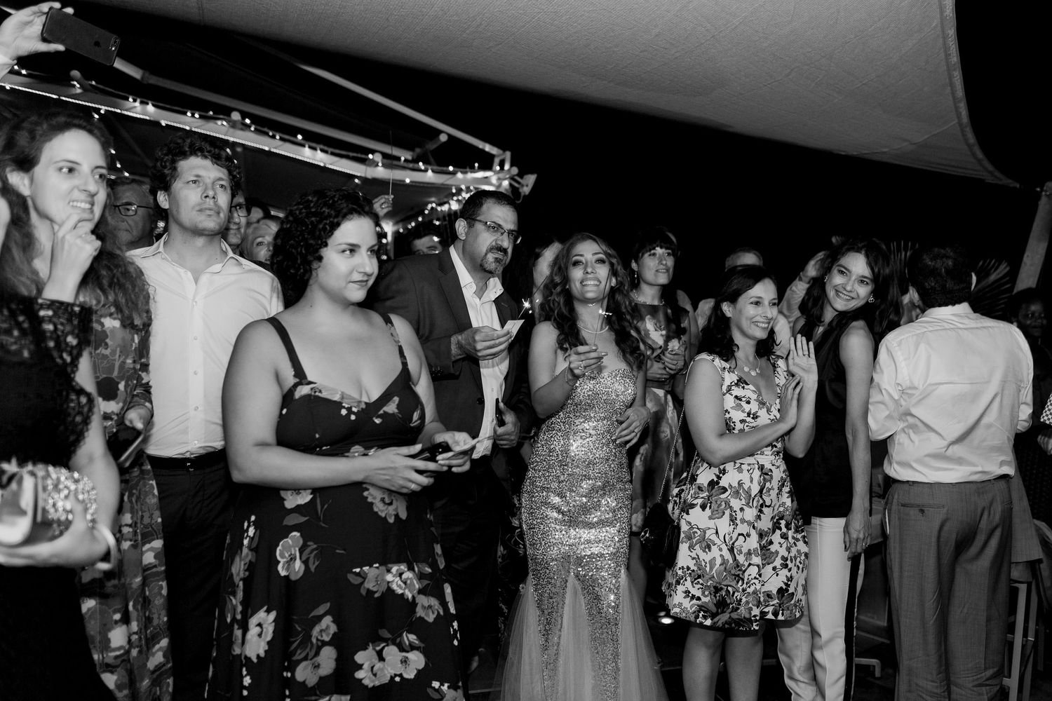Photo en noir et blanc d'invités de mariage élégamment vêtus, en train de converser et d'observer la scène lors d'une réception en plein air
