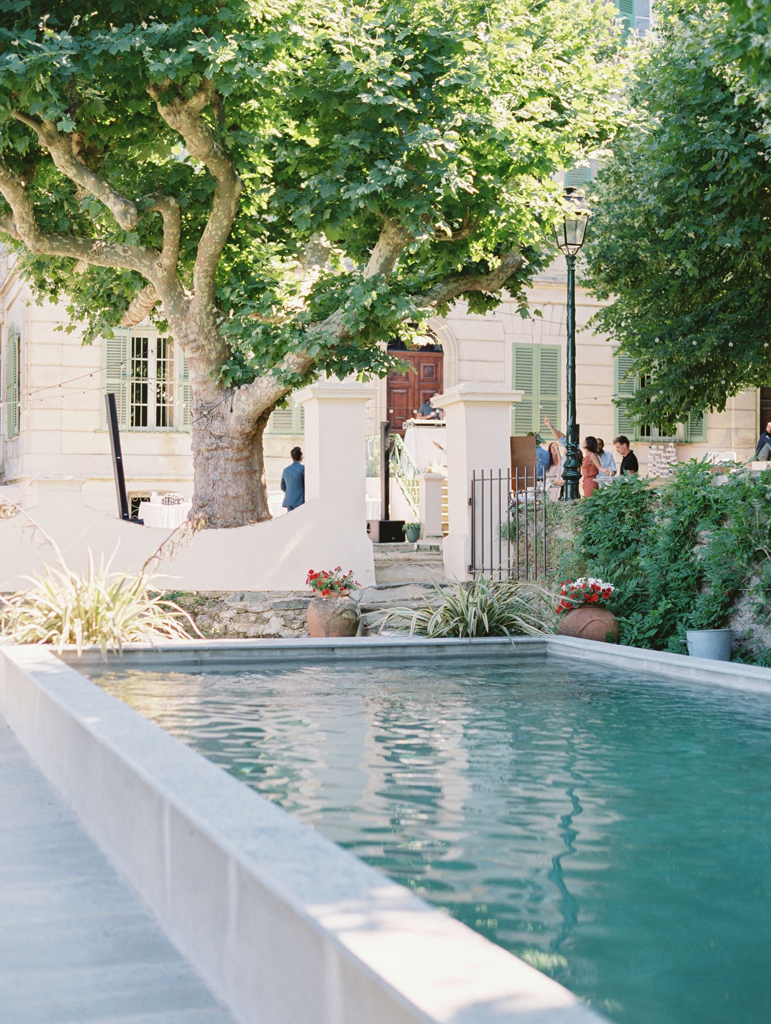 Elegant outdoor pool surrounded by lush trees and guests at a European estate venue.