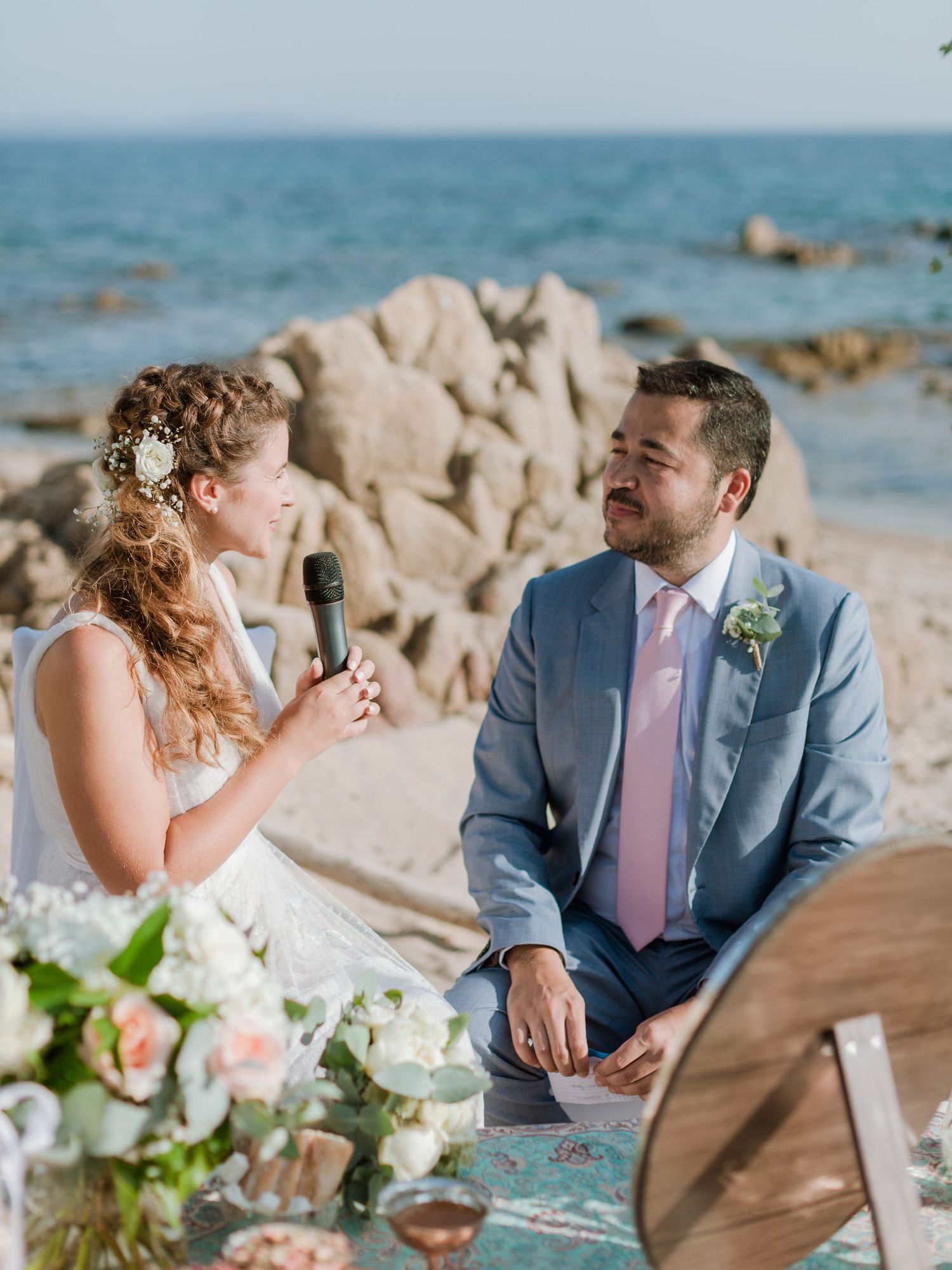 La mariée lit ses vœux au marié lors d'une cérémonie de mariage romantique en bord de mer, agrémentée de compositions florales