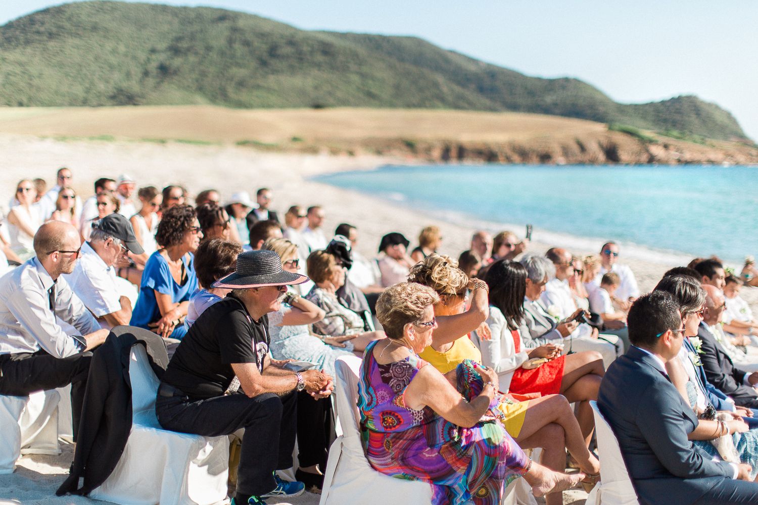 Les invités sont assis sur des chaises blanches, sur une plage de sable fin, lors d'une cérémonie de mariage en plein air avec vue sur l'eau