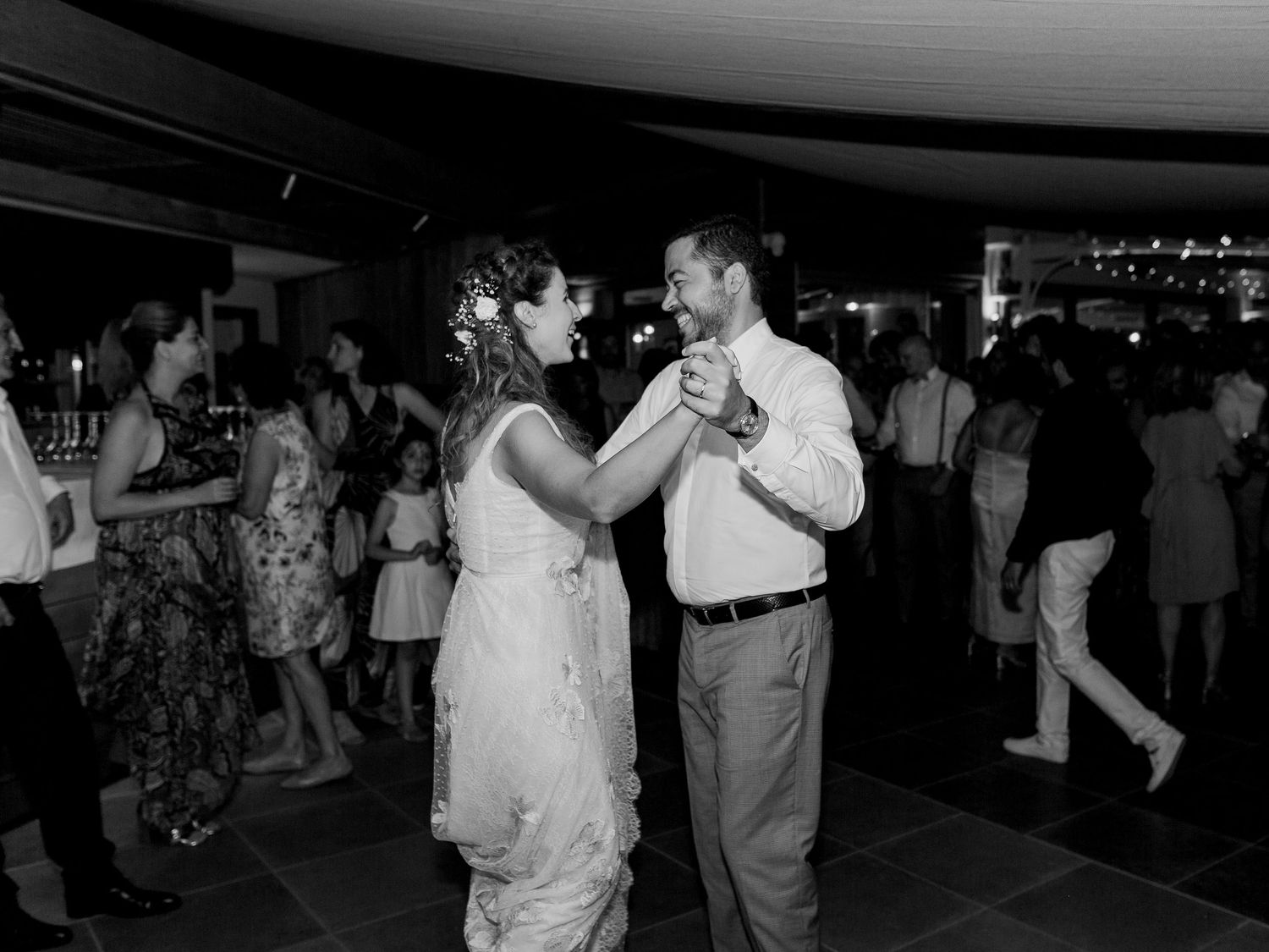 Photo en noir et blanc d'un couple partageant une première danse romantique lors d'une réception de mariage, avec des invités