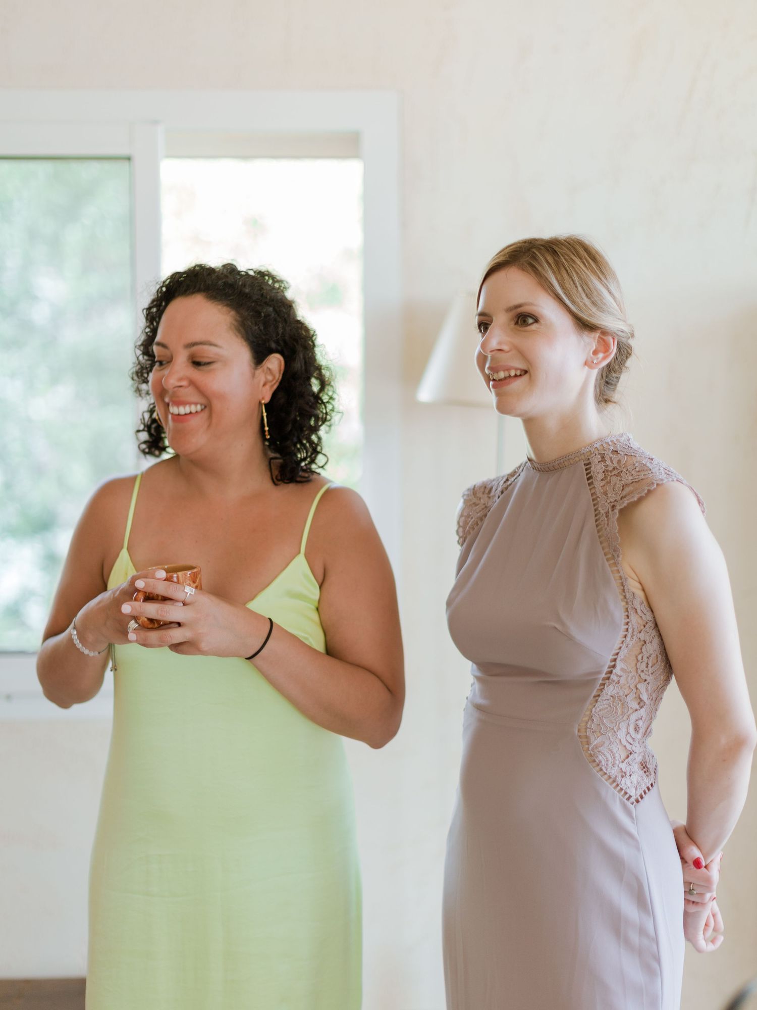 Deux femmes en robes élégantes riant ensemble lors d'un événement mondain, l'une en vert et l'autre en taupe.