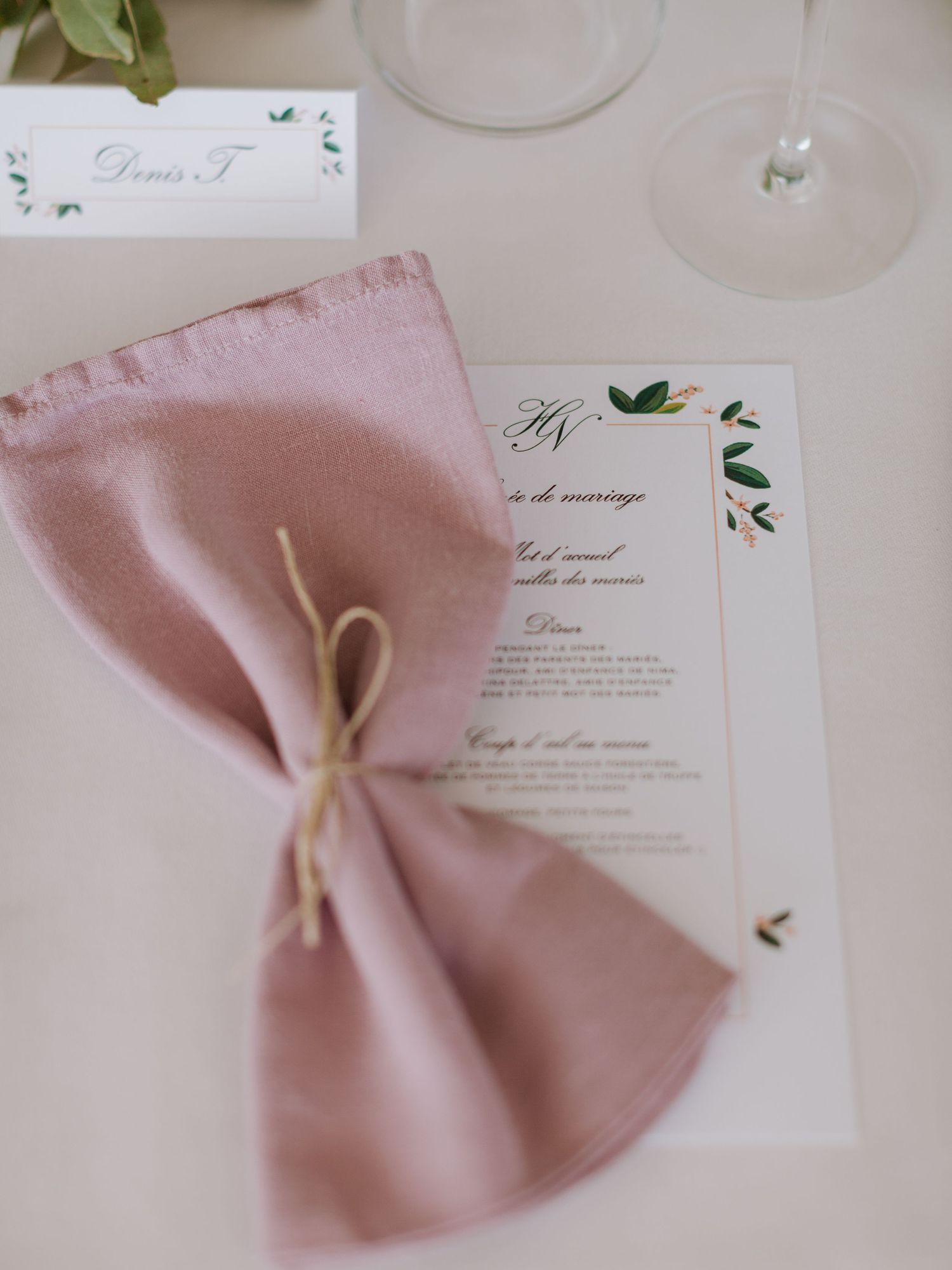 Élégant dressage de table de mariage avec une serviette en lin vieux rose, une carte de menu fleurie et un marque-place sur une nappe blanch