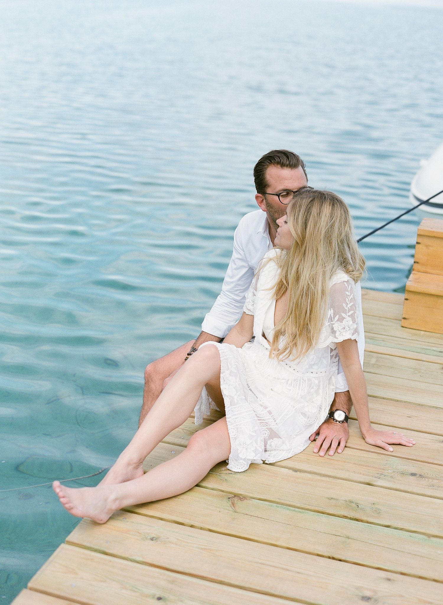 Un couple romantique s'embrasse, assis sur une jetée en bois ensoleillée, au bord d'une eau bleue et calme au Maora Beach Bonifacio.