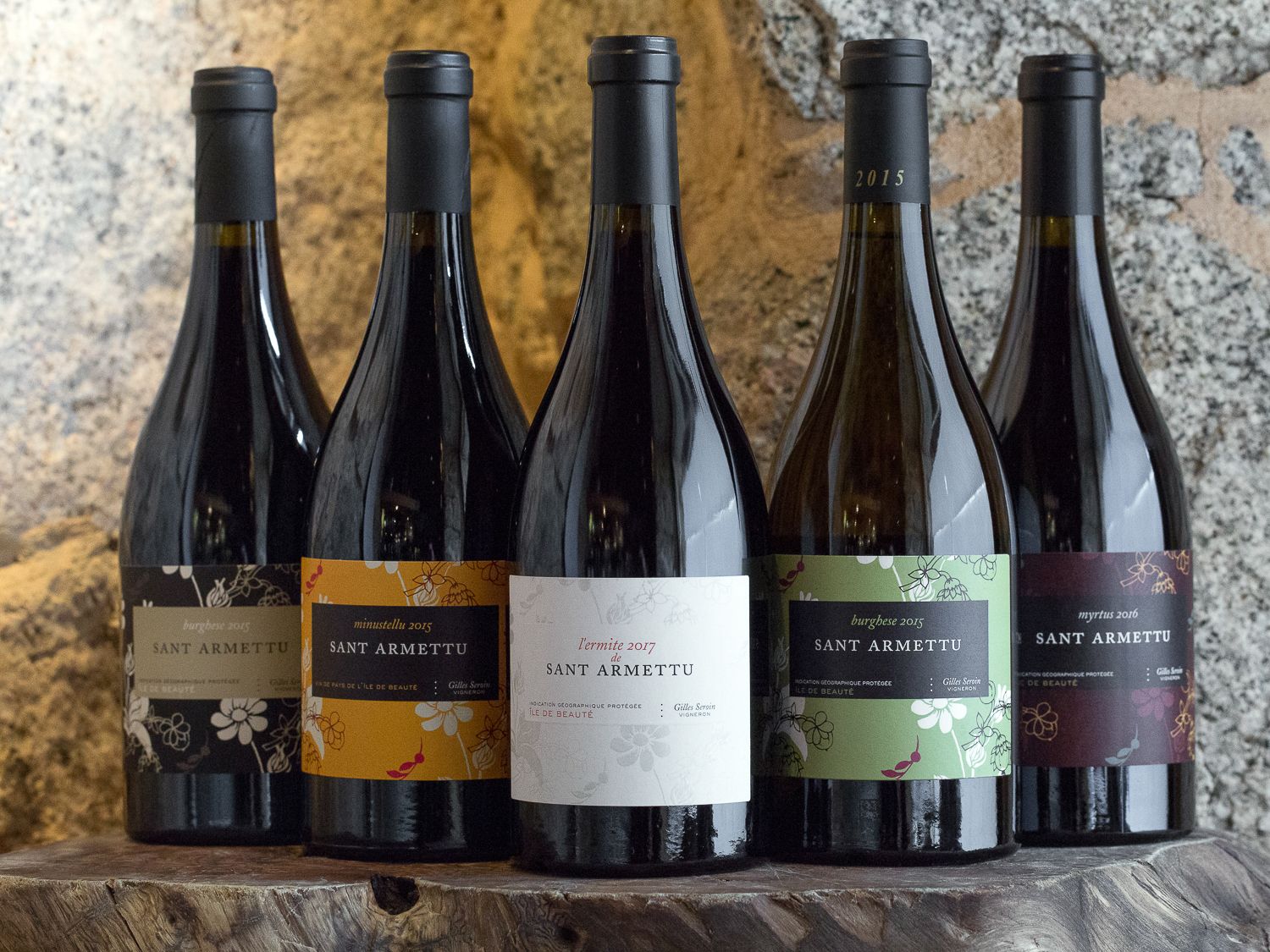 Cinq bouteilles de vin corse Sant Armettu présentées sur une surface en bois devant un fond en pierre.