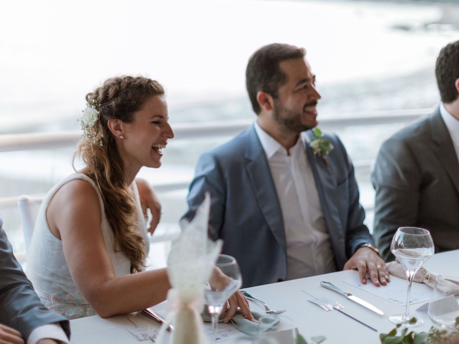 Les mariés rient ensemble à la table de la réception, avec l'océan en toile de fond.