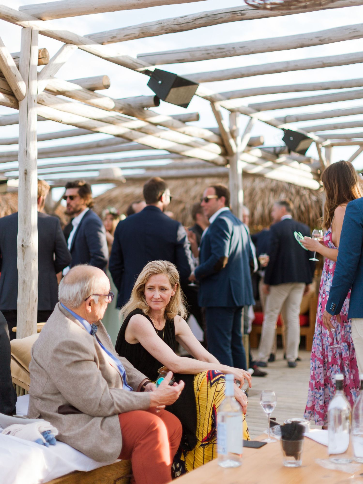Les invités se mêlent et se détendent lors d'une élégante réception de mariage en plein air sur la plage, sous une pergola en bois.