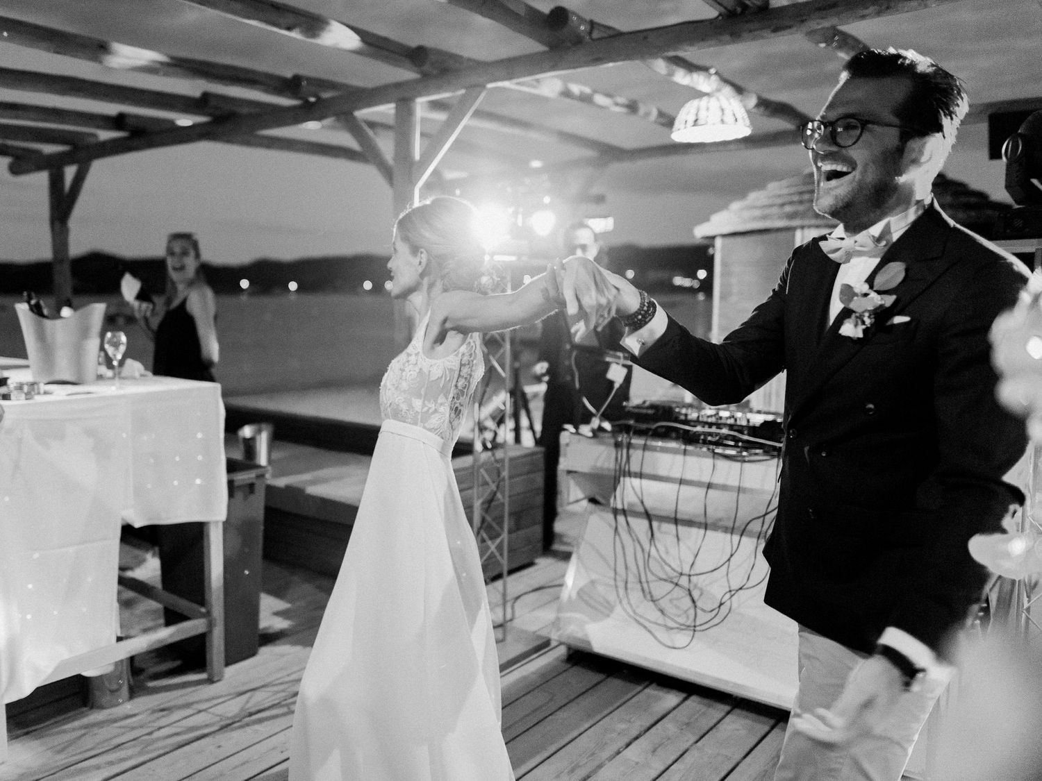 Photo en noir et blanc d'une mariée et d'un marié dansant joyeusement sur une terrasse en bois lors de leur réception de mariage