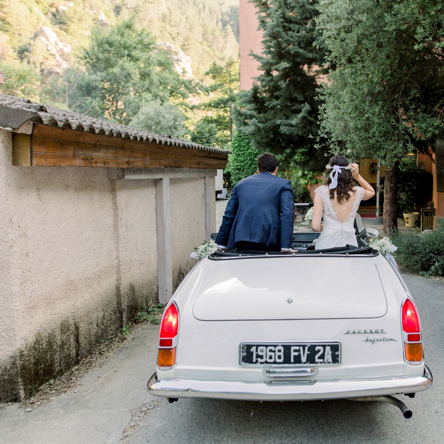 Bride and groom driving away in a vintage white 1968 convertible car on their wedding day.