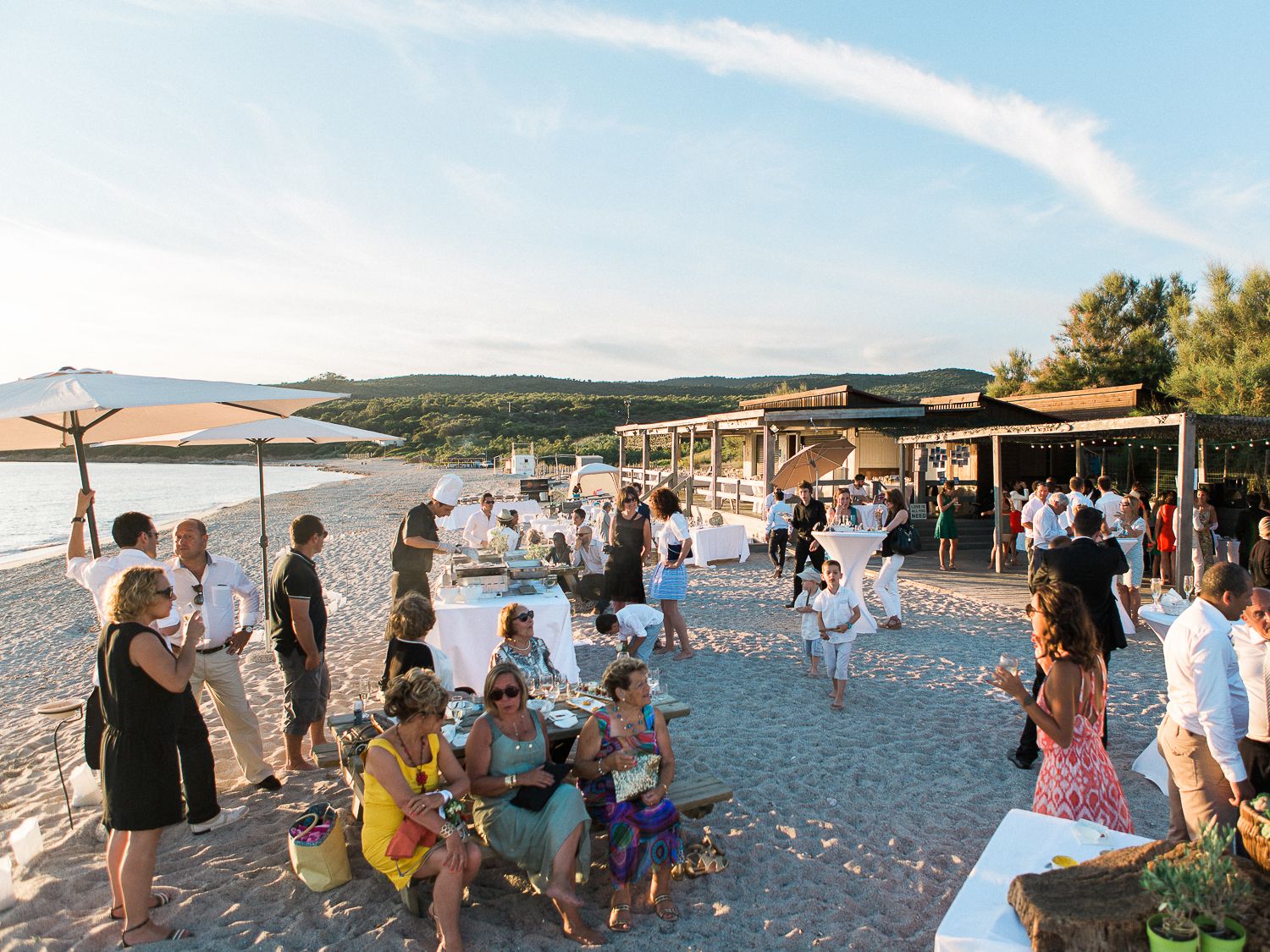 Des invités se retrouvent dans un lieu événementiel extérieur en bord de mer, avec une vue imprenable sur le coucher de soleil.