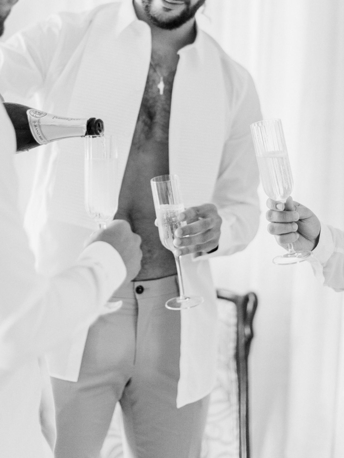Photo en noir et blanc d'un marié se faisant verser du champagne dans sa flûte tout en tenant un autre verre avant son mariage.
