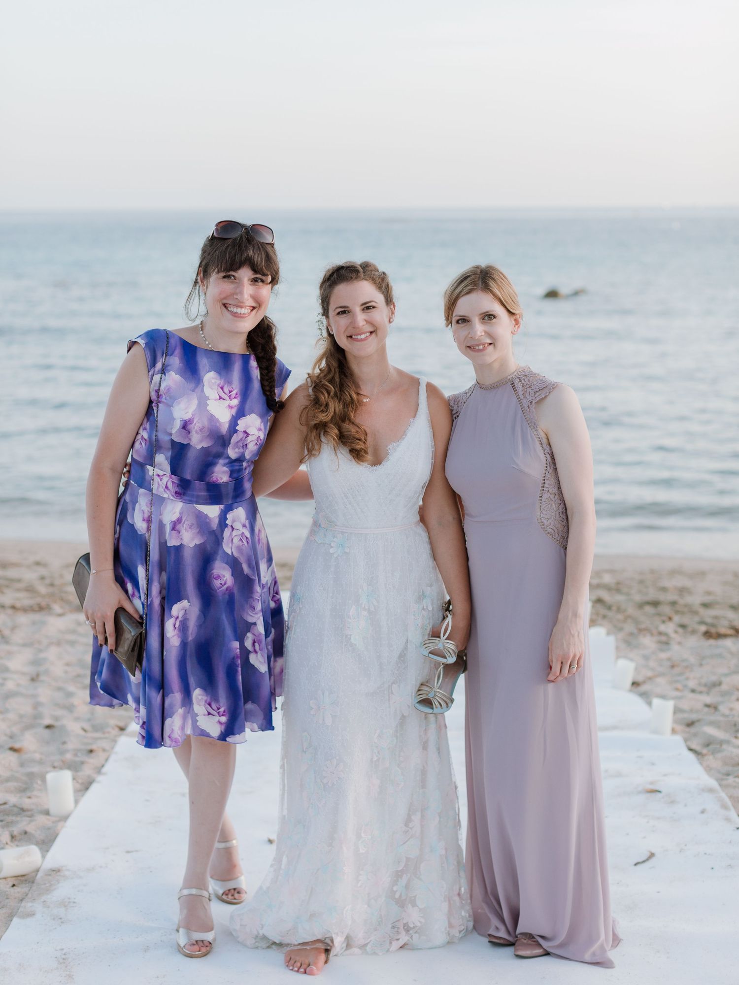 Trois femmes posant sur une plage : l'une porte une robe de mariée blanche et est entourée d'invitées vêtues de robes bleues