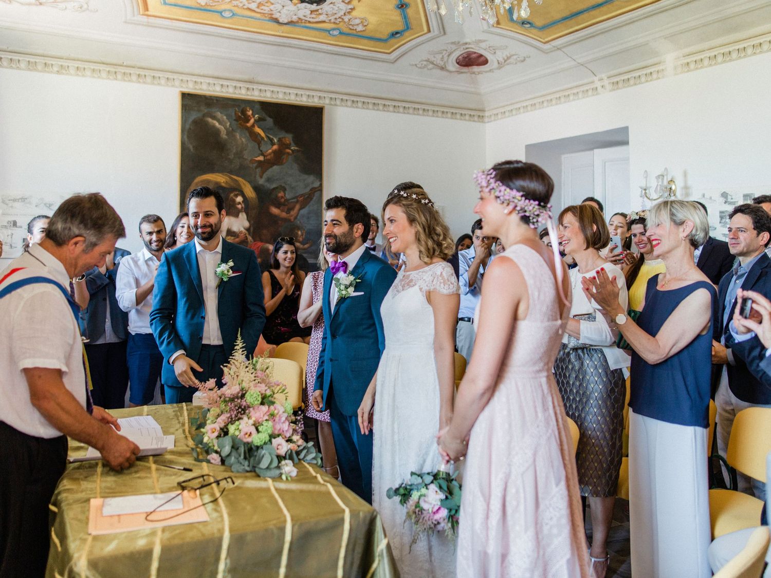Elegant wedding ceremony in ornate hall with bride, groom, and guests gathered around signing table.