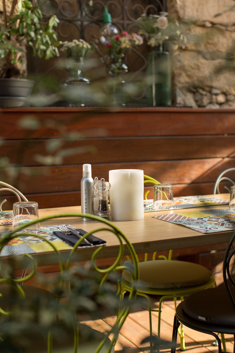 Table de restaurant en plein air dressée avec bougie, moulins à sel et à poivre et sets de table colorés sur une terrasse en bois.