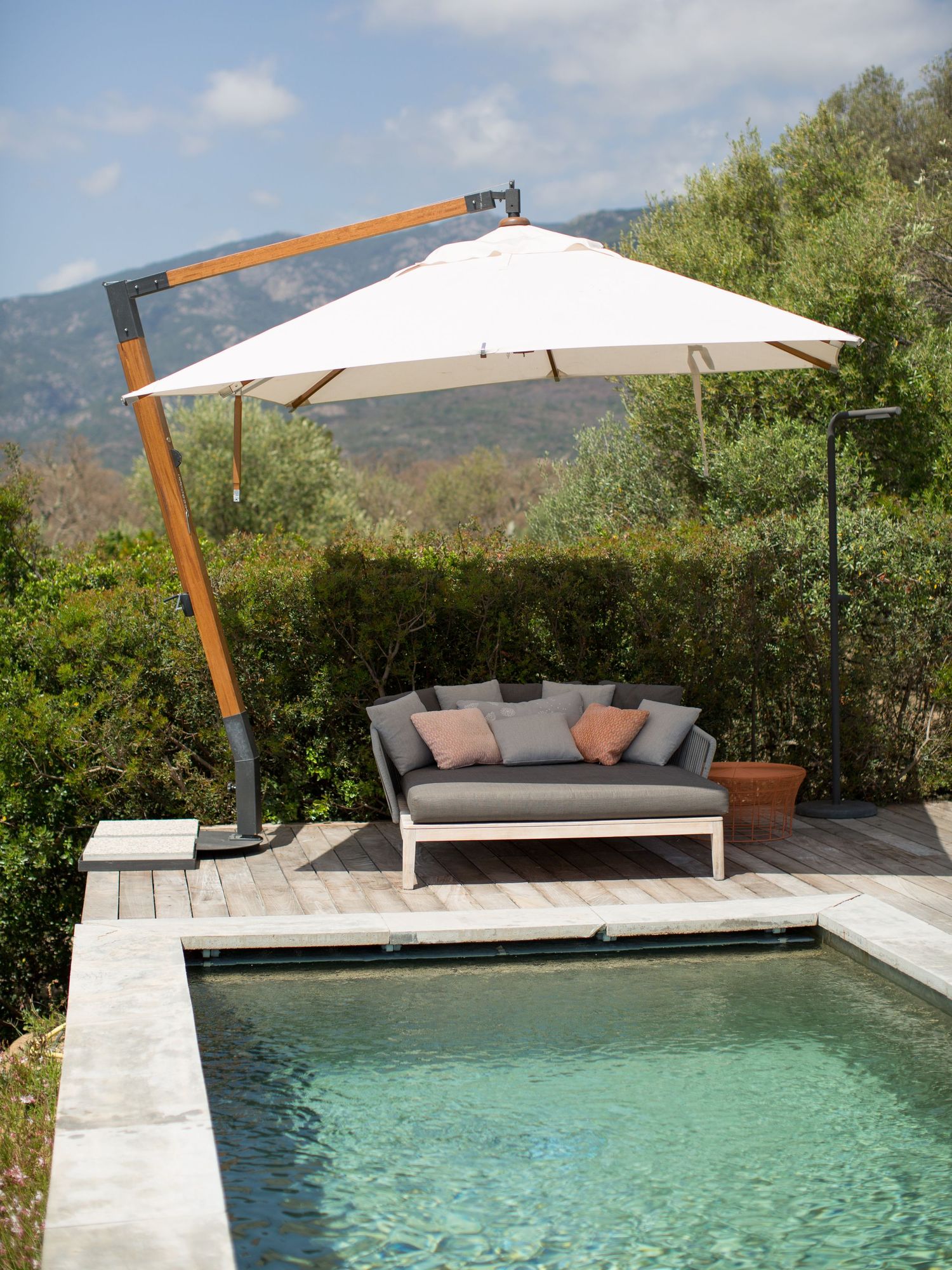 Élégante terrasse au bord de la piscine, avec un grand parasol blanc en porte-à-faux et vue sur les montagnes. Photoshoot à Porto-vecchio.