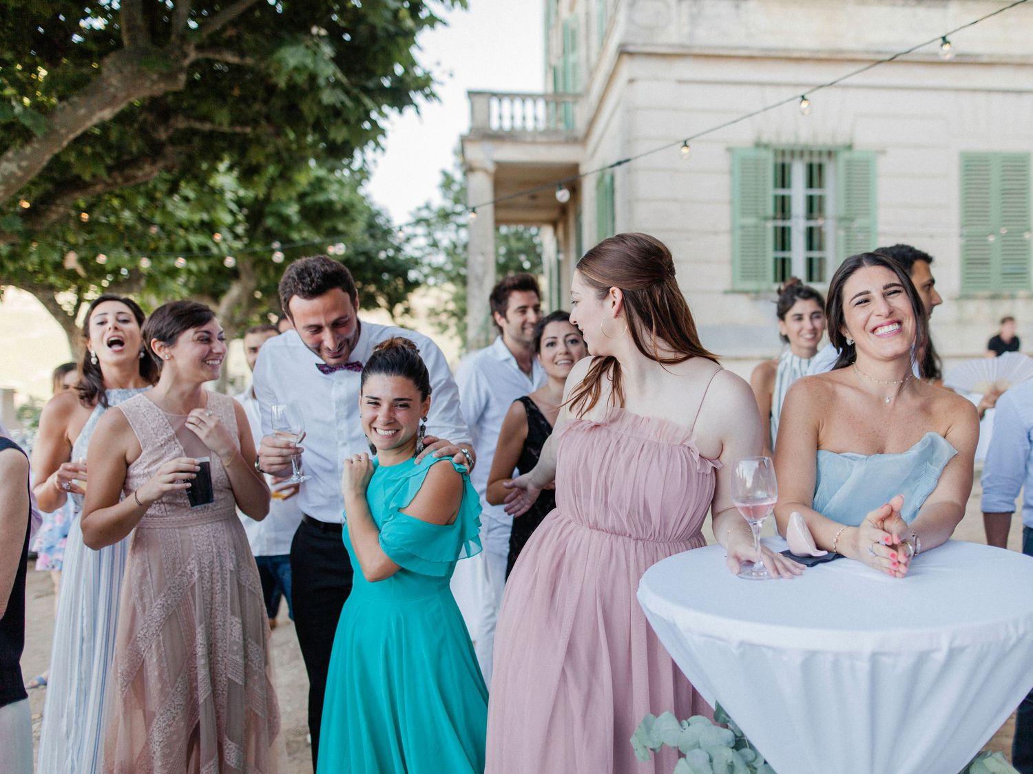 Wedding guests laughing and celebrating outdoors at an elegant venue with bridesmaids in colorful dresses.