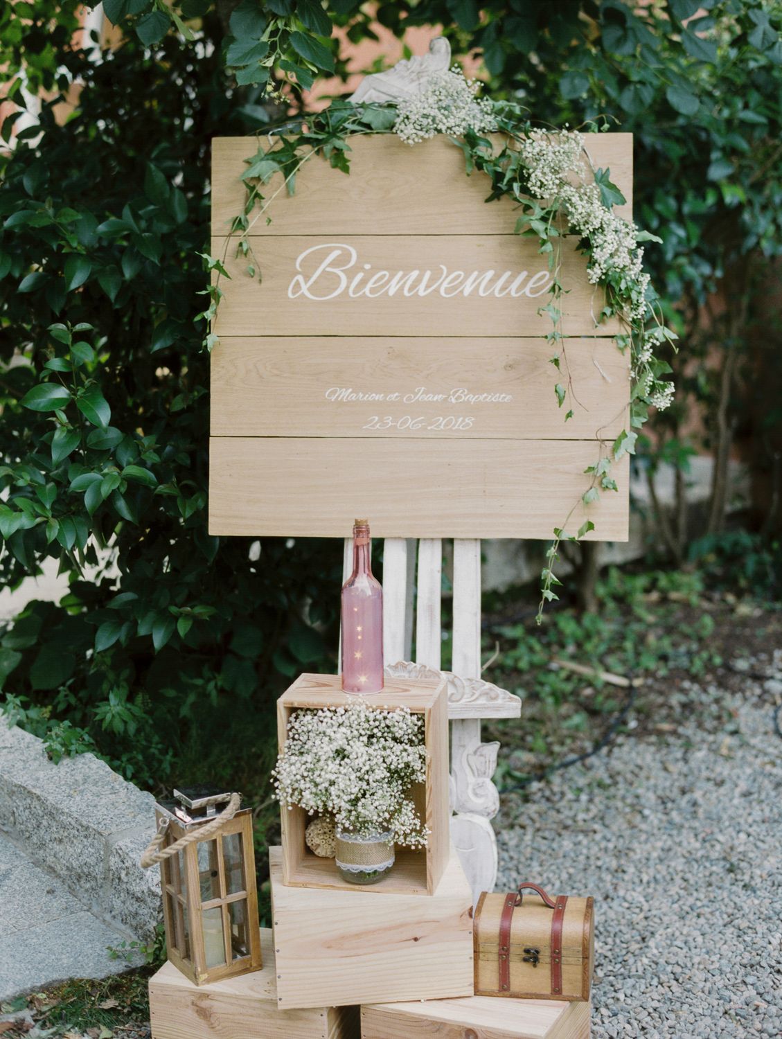 Rustic wedding welcome sign reading Bienvenue on wooden pallet with greenery, baby's breath, and decorative crates.