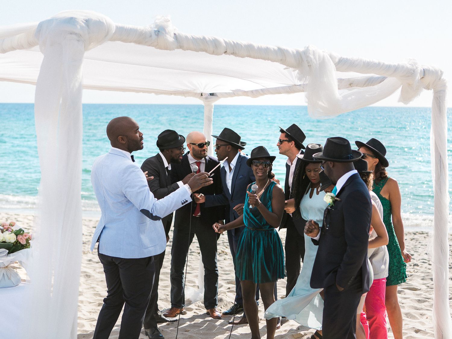 Un groupe d'invités élégamment vêtus se rassemble sous un dais blanc pour une cérémonie de mariage sur la plage, au bord de l'océan.