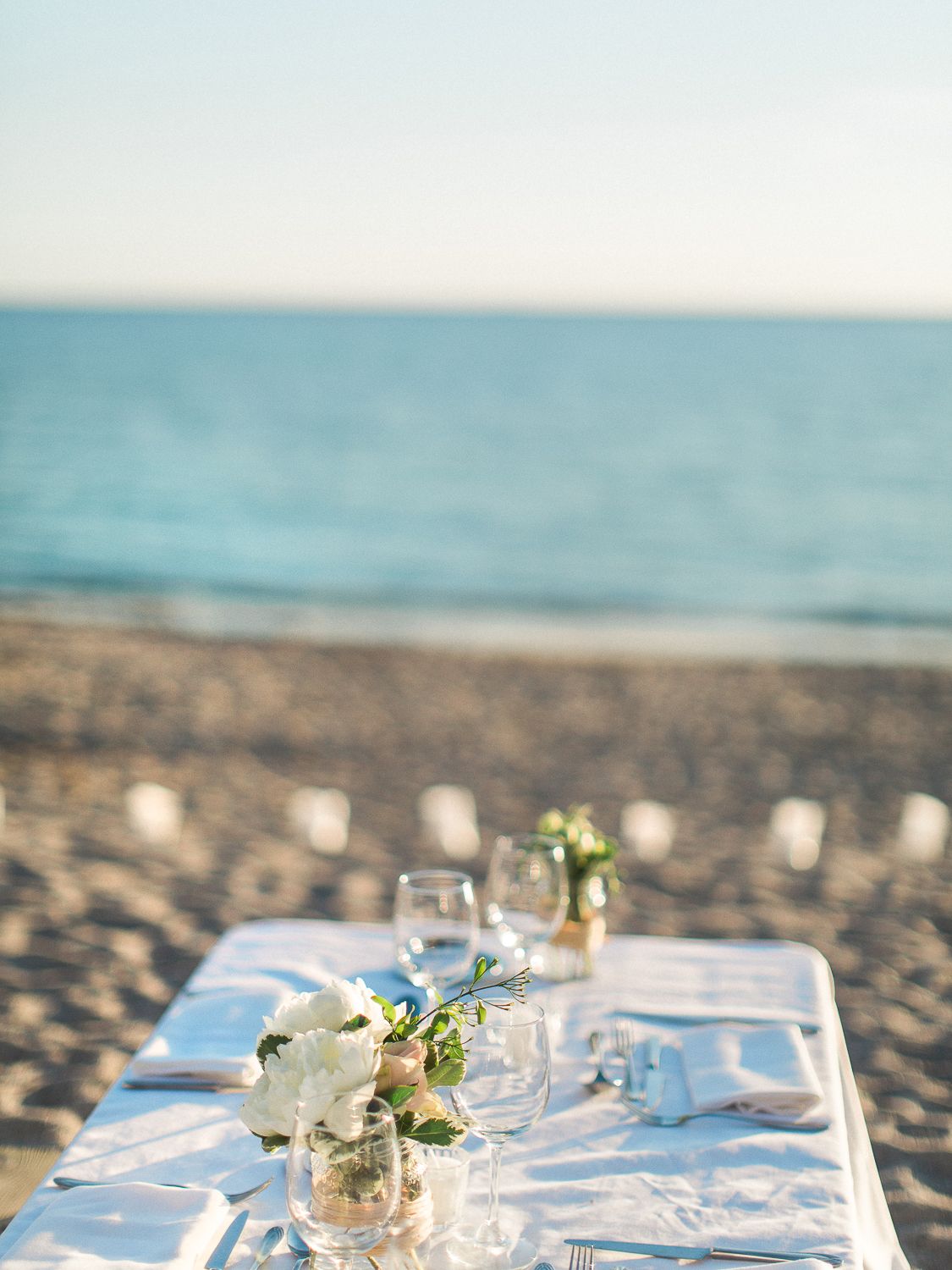Élégante décoration de table pour un mariage sur la plage, avec des centres de table floraux blancs, de la verrerie et la mer