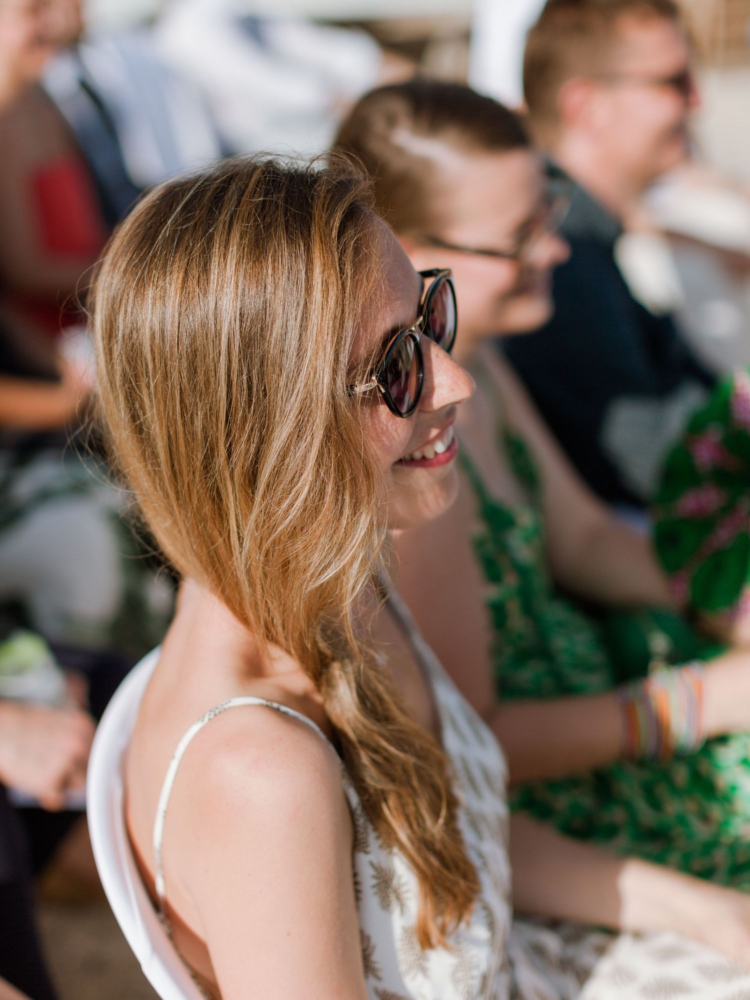 Jeune femme aux longs cheveux blonds portant des lunettes de soleil et souriant lors d'un événement estival en plein air.