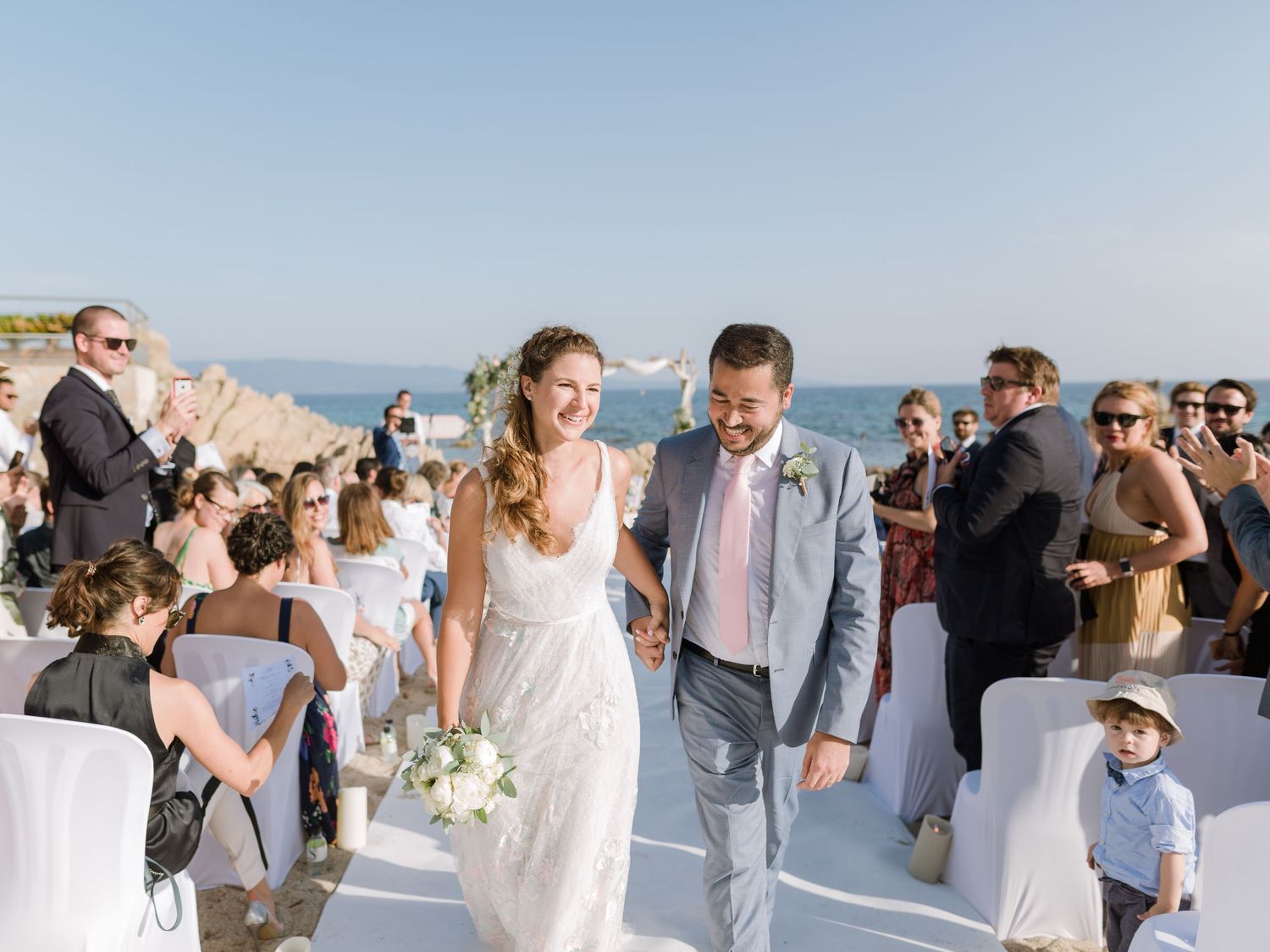 Les mariés parcourent l'allée en plein air au bord de l'océan après la cérémonie sur la plage, sous les acclamations des invités