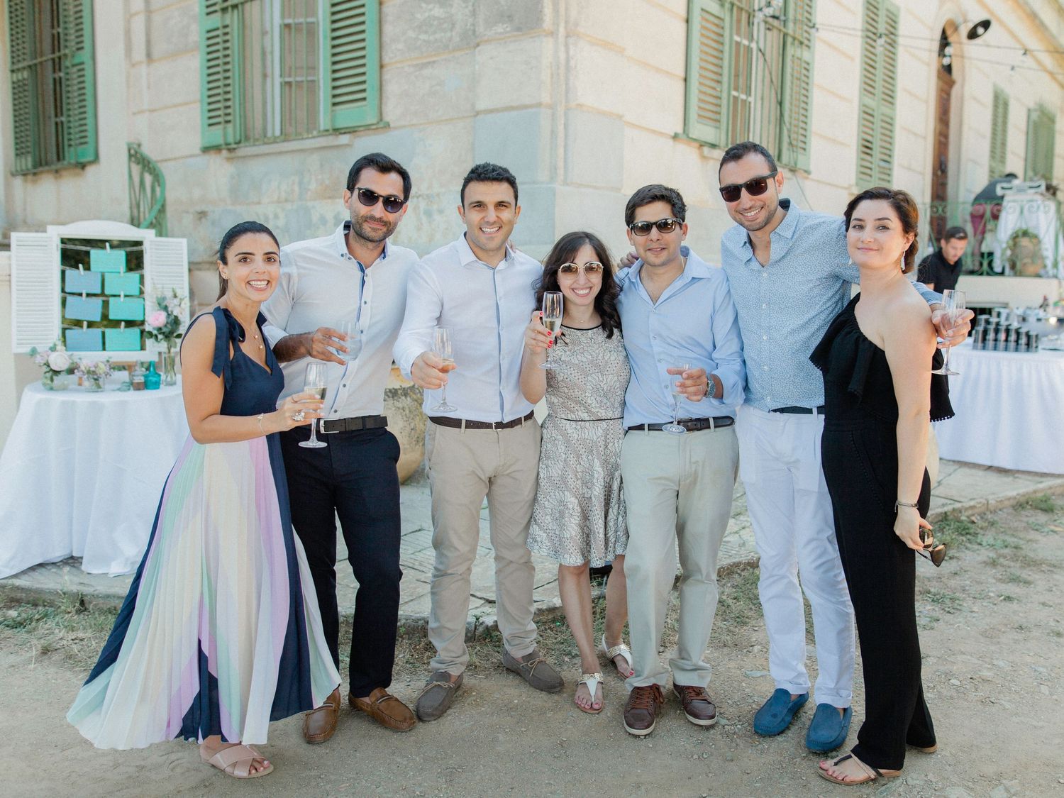 Group of seven friends posing together at an outdoor wedding reception near a historic building.