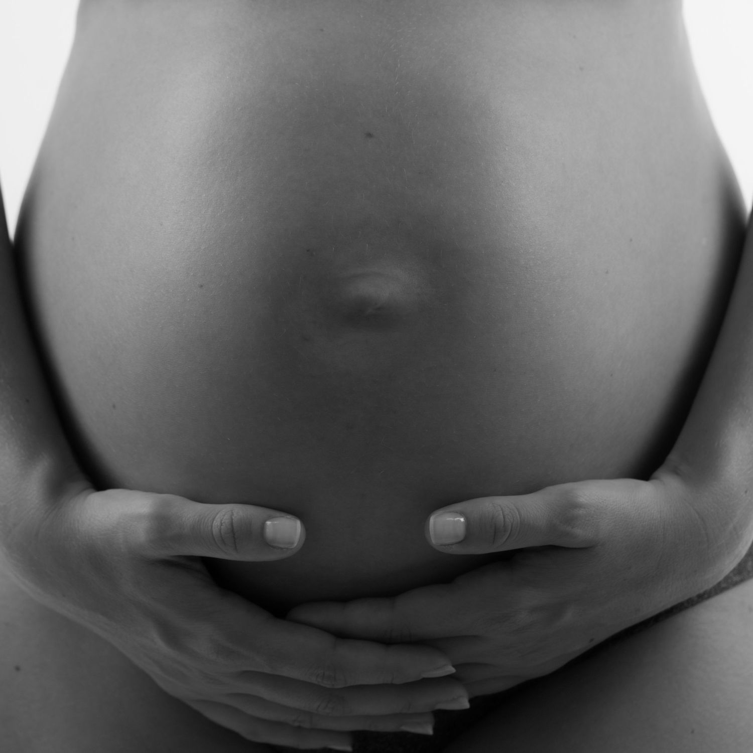 Photo en gros plan, en noir et blanc, d'une femme enceinte berçant son ventre nu à deux mains.