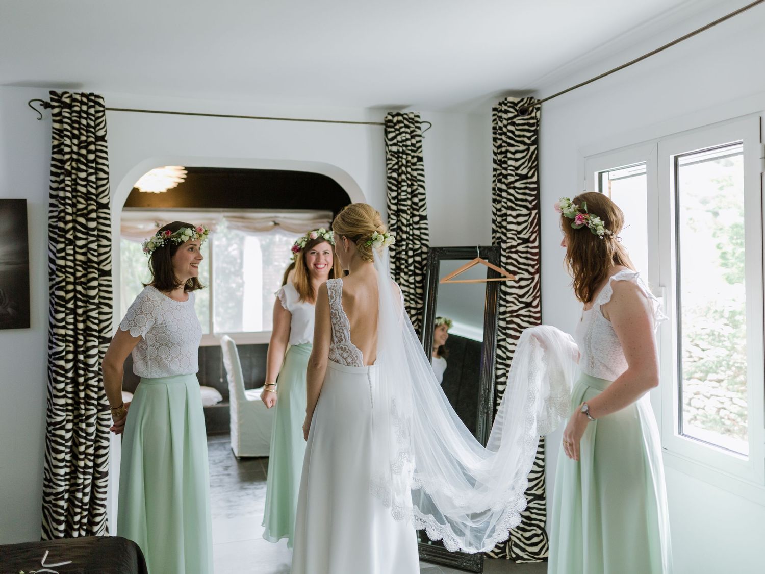 La mariée en robe blanche, entourée de ses demoiselles d'honneur en robes menthe, ajuste sa traîne avant la cérémonie de mariage.