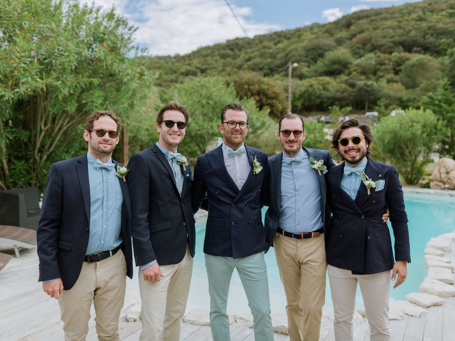 Cinq garçons d'honneur en blazers bleu marine et pantalons kaki posent ensemble à l'extérieur, près d'une piscine