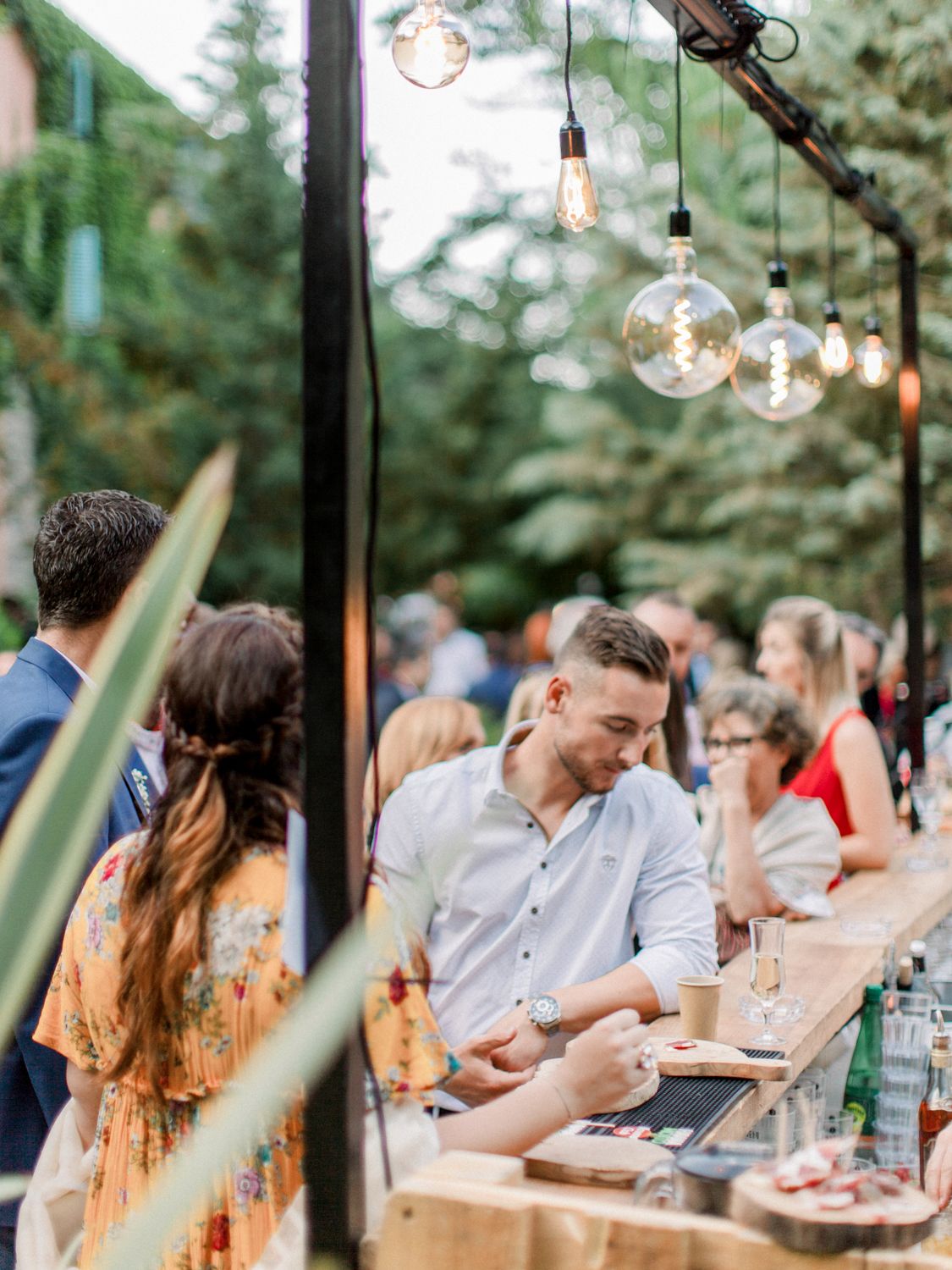 Les invités se mêlent aux convives autour d'un bar extérieur éclairé par des ampoules Edison lors d'une élégante garden-party à Corte