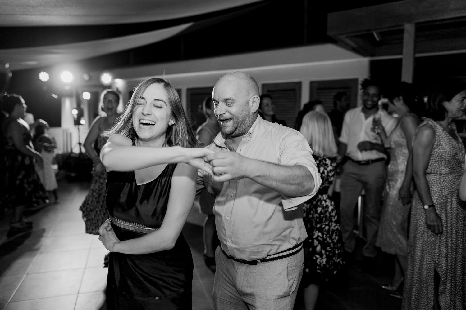 Photo en noir et blanc d'un couple dansant joyeusement ensemble lors d'une réception de mariage animée.