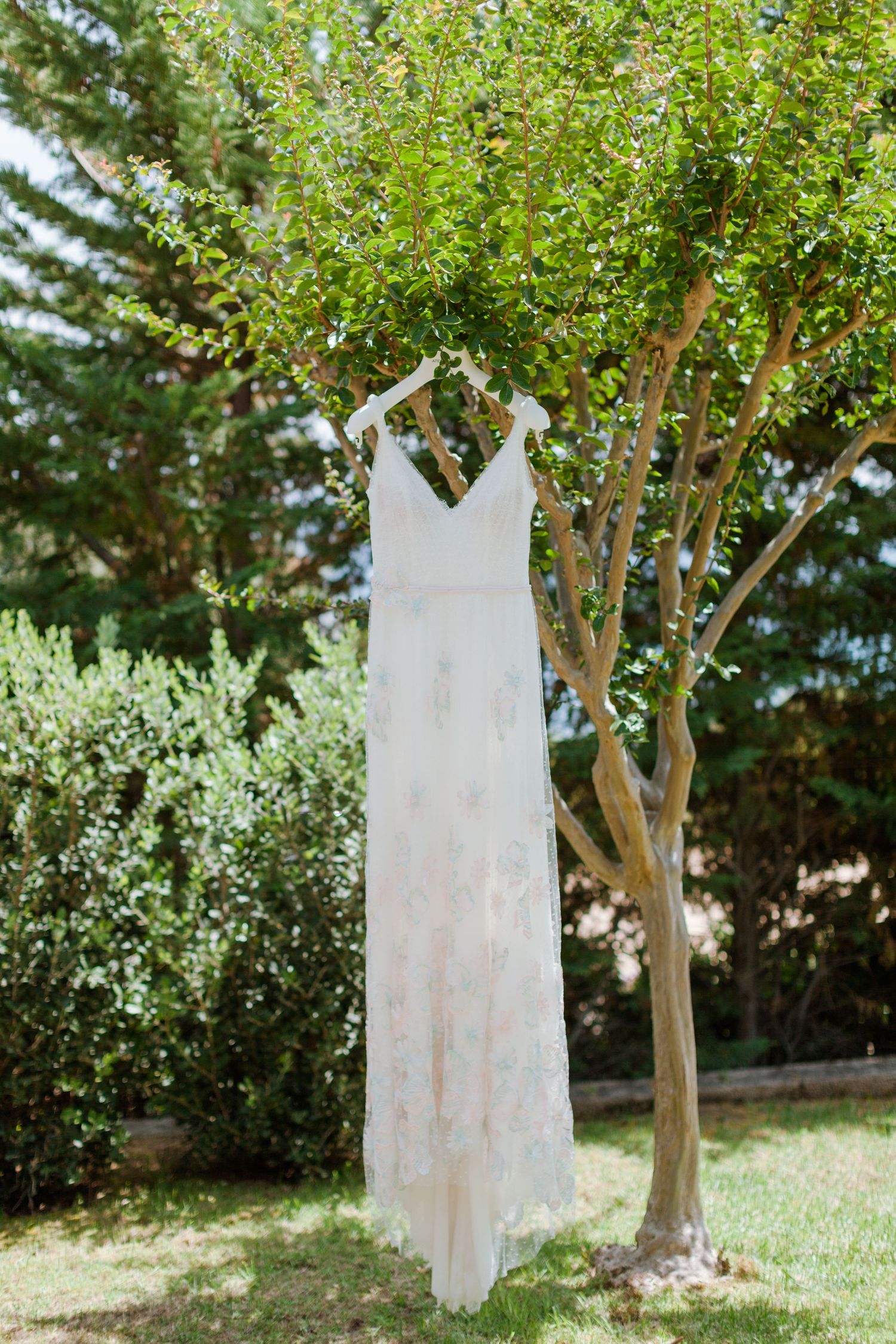Élégante robe de mariée en dentelle blanche suspendue à une branche d'arbre, en extérieur, dans un jardin verdoyant.