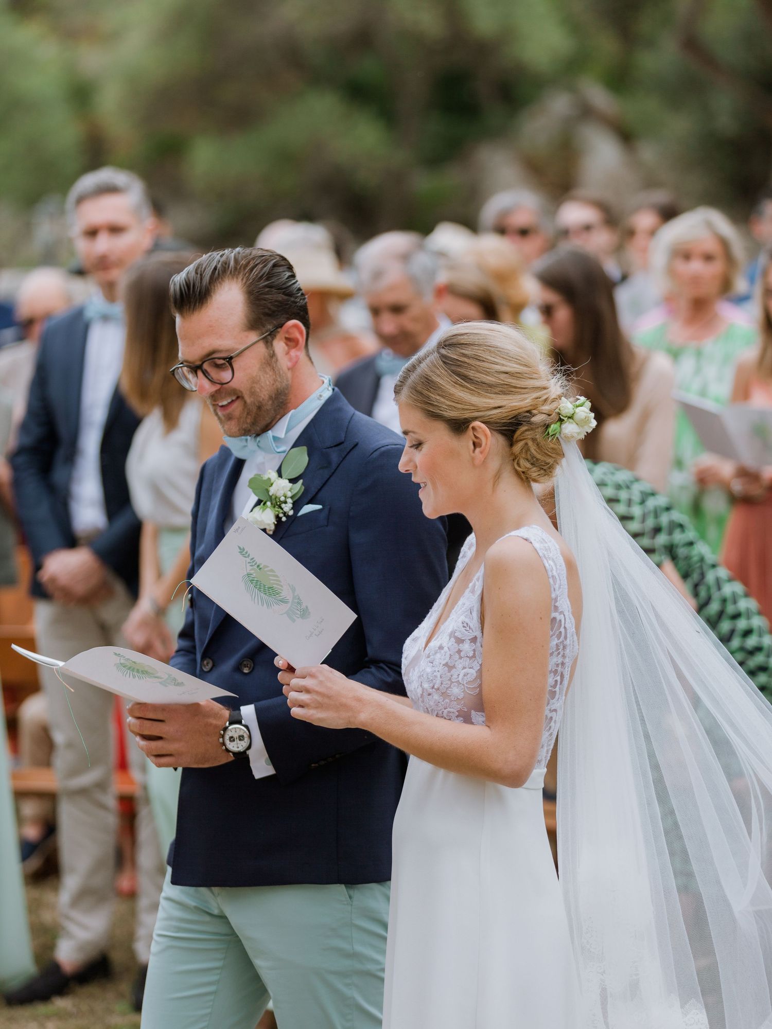 Les mariés échangent leurs vœux lors d'une cérémonie en plein air, la mariée en robe blanche avec voile, le marié en costume bleu marine.