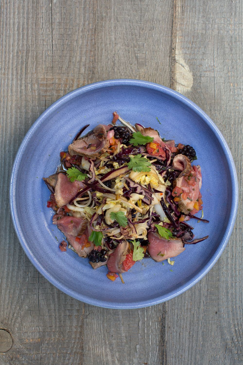 Salade de canard gastronomique avec riz noir, chou, tomates et herbes fraîches, servie dans une assiette en céramique bleue.