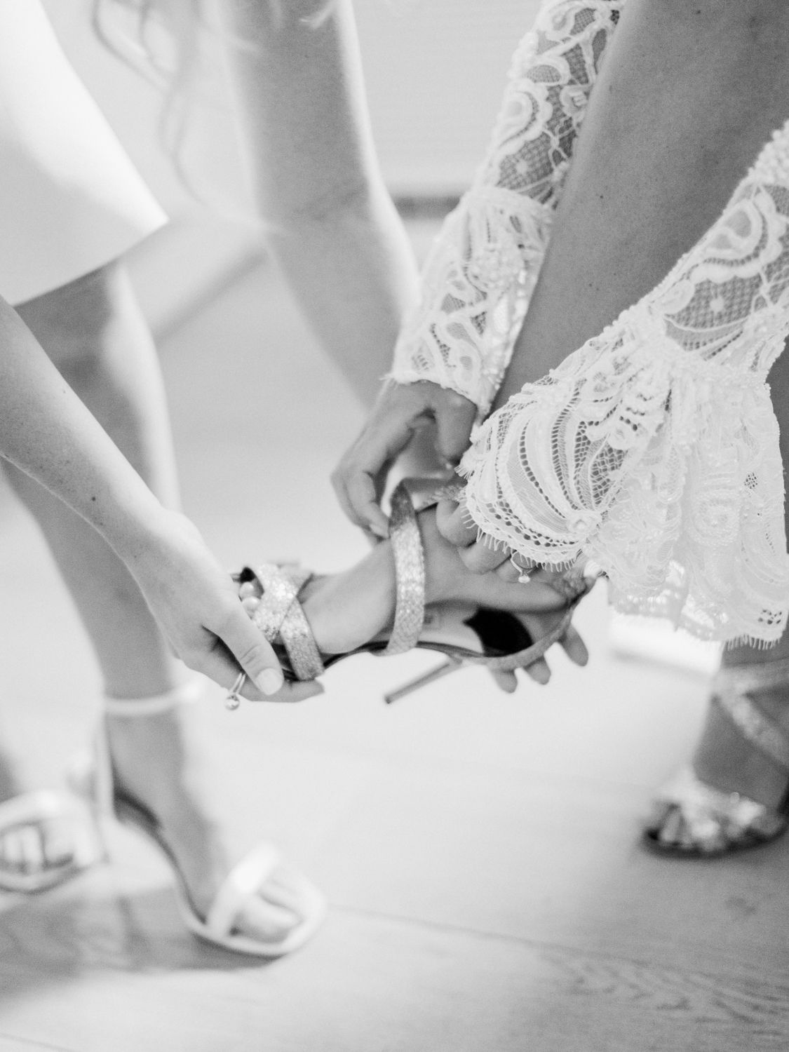 Une demoiselle d'honneur aide la mariée à enfiler ses chaussures de mariage à talons et brides, photo en gros plan en noir et blanc.
