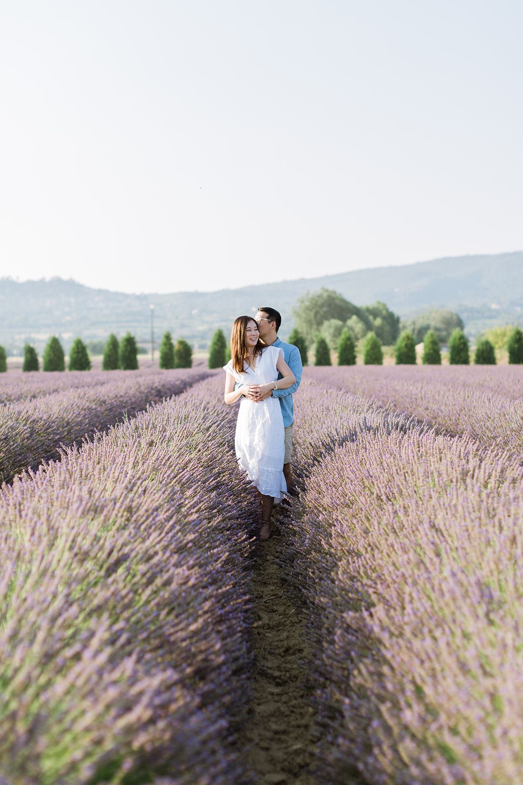 Un couple s'embrasse dans un vaste champ de lavande violette, avec les montagnes en arrière-plan à Gordes en Provence.