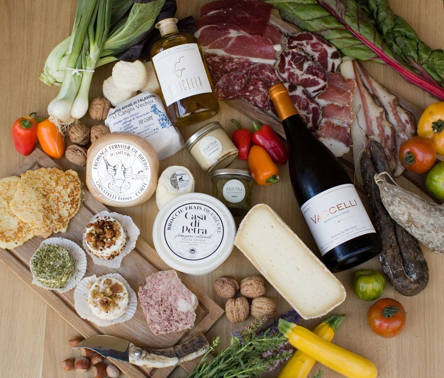 Planche de charcuterie rustique avec assortiment de fromages, charcuteries, légumes frais, noix, huile d'olive et vin rouge à L'orriu.